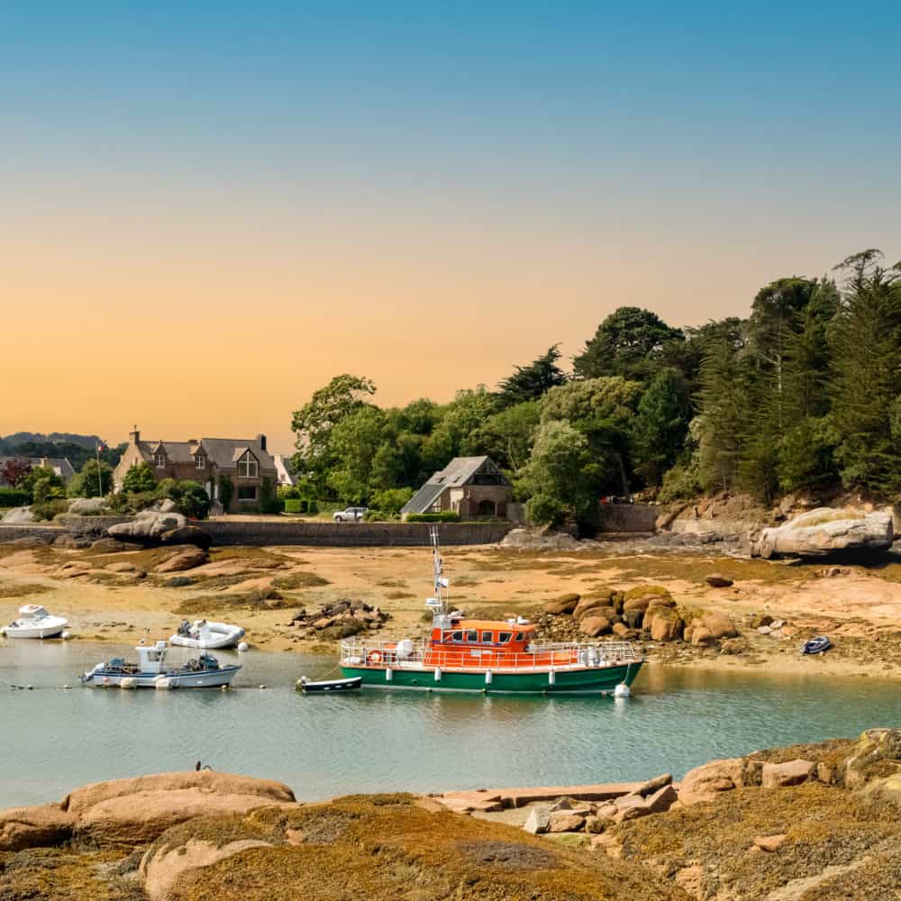 pink granite coast (cote de granite rose) at sunset. yachts and boats in the harbor at low tide. ploumanach, perros guirec, brittany, france.